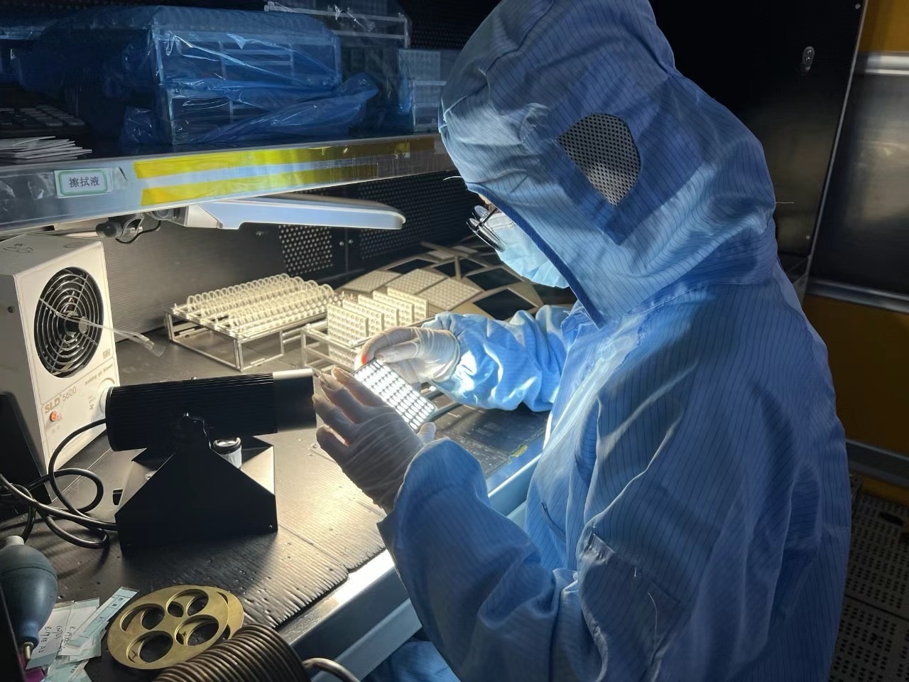Gloved operator viewing a clear rectangular component with repeated features under a bright inspection light